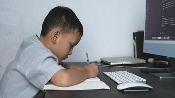 a boy is learning to do his schoolwork in front of a computer by writing on his book video
