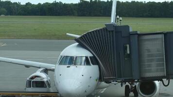 Passenger airplane docked at airport gate with connected jet bridge and ground support vehicle. Passengers boarding white airplane video