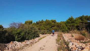Man running on a rocky path surrounded by nature, suffering from knee pain during exercise under clear blue sky video