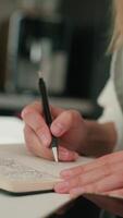 Person is sketching in notebook while working remotely at desk with laptop. Freelance work at home office. Graphic designer drawing sketch video