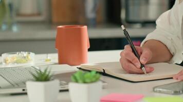 Person is sketching in notebook while working remotely at desk with laptop. Freelance work at home office. Graphic designer drawing sketch video