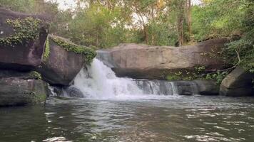 waterfall flowing over smooth, rocky terrain surrounded by lush green forest, The crystal-clear water cascades gently into a calm river below, creating a peaceful and natural, landscape video