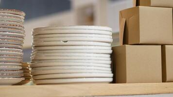 A neatly arranged stack of clean white plates placed alongside cardboard boxes on a shelf video