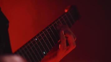 Close-up of the hands of the guitarist playing chords on the guitar fretboard while performing a cheerful rock song on the show under red concert lights video