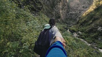 First person view of a young woman with a backpack leads by the hand during a walk together on the mountain trail between dense grass. Concept of active outdoor hike tourism video