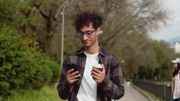 Young man using smartphone while walking in a park video