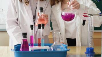 Two students in lab coats examine liquids in flasks in slow motion video