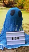 Halloween holiday concept. Handmade blue ghost made from bandages and glue with Lightbox BOO text in autumn forest background. Children's art project. DIY concept. video