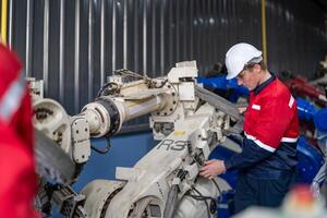 male engineer workers maintenance automatic robotic arm machine in a factory. worker checking and repairing automatic robot hand machine. photo