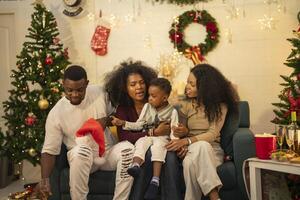 A lively Christmas celebration with three african friends enjoying drinks and holiday cheer on a sofa. The festive atmosphere includes Christmas trees, wreaths, lights, and decorations. photo