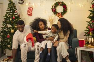 A lively Christmas celebration with three african friends enjoying drinks and holiday cheer on a sofa. The festive atmosphere includes Christmas trees, wreaths, lights, and decorations. photo
