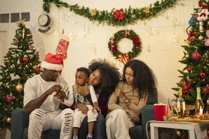 A lively Christmas celebration with three african friends enjoying drinks and holiday cheer on a sofa. The festive atmosphere includes Christmas trees, wreaths, lights, and decorations. photo