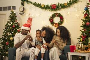 A lively Christmas celebration with three african friends enjoying drinks and holiday cheer on a sofa. The festive atmosphere includes Christmas trees, wreaths, lights, and decorations. photo