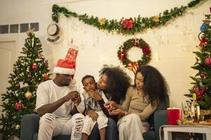 A lively Christmas celebration with three african friends enjoying drinks and holiday cheer on a sofa. The festive atmosphere includes Christmas trees, wreaths, lights, and decorations. photo