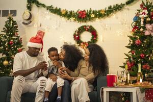 A lively Christmas celebration with three african friends enjoying drinks and holiday cheer on a sofa. The festive atmosphere includes Christmas trees, wreaths, lights, and decorations. photo