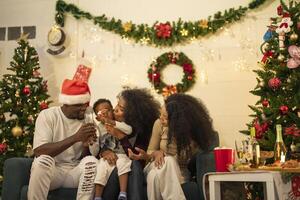 A lively Christmas celebration with three african friends enjoying drinks and holiday cheer on a sofa. The festive atmosphere includes Christmas trees, wreaths, lights, and decorations. photo