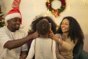 A lively Christmas celebration with three african friends enjoying drinks and holiday cheer on a sofa. The festive atmosphere includes Christmas trees, wreaths, lights, and decorations. photo