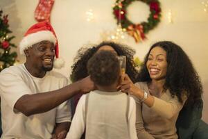 A lively Christmas celebration with three african friends enjoying drinks and holiday cheer on a sofa. The festive atmosphere includes Christmas trees, wreaths, lights, and decorations. photo