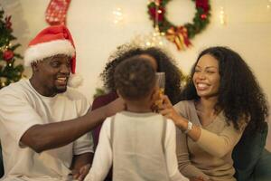 A lively Christmas celebration with three african friends enjoying drinks and holiday cheer on a sofa. The festive atmosphere includes Christmas trees, wreaths, lights, and decorations. photo