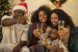 A lively Christmas celebration with three african friends enjoying drinks and holiday cheer on a sofa. The festive atmosphere includes Christmas trees, wreaths, lights, and decorations. photo