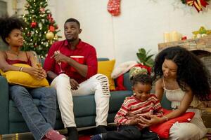 A family enjoying a cozy Christmas evening at home. The group gathers around the Christmas tree, sharing laughs and stories. The warmth of the festive season is felt as they relax and bond together. photo