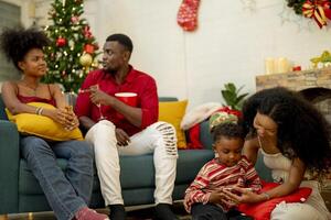A family enjoying a cozy Christmas evening at home. The group gathers around the Christmas tree, sharing laughs and stories. The warmth of the festive season is felt as they relax and bond together. photo