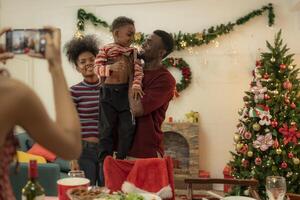 A joyful family gathers around the dinner table celebrating Christmas. The father, dressed in a Santa hat, gives a gift to the child, while everyone smiles with warmth and festive decorations. photo