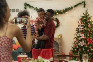 A joyful family gathers around the dinner table celebrating Christmas. The father, dressed in a Santa hat, gives a gift to the child, while everyone smiles with warmth and festive decorations. photo