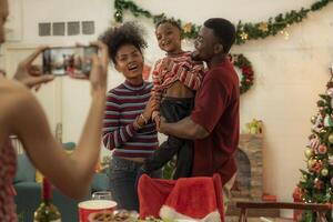 A joyful family gathers around the dinner table celebrating Christmas. The father, dressed in a Santa hat, gives a gift to the child, while everyone smiles with warmth and festive decorations. photo