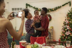 A joyful family gathers around the dinner table celebrating Christmas. The father, dressed in a Santa hat, gives a gift to the child, while everyone smiles with warmth and festive decorations. photo
