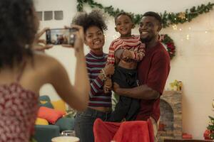 A joyful family gathers around the dinner table celebrating Christmas. The father, dressed in a Santa hat, gives a gift to the child, while everyone smiles with warmth and festive decorations. photo