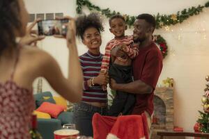 A joyful family gathers around the dinner table celebrating Christmas. The father, dressed in a Santa hat, gives a gift to the child, while everyone smiles with warmth and festive decorations. photo