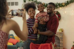 A joyful family gathers around the dinner table celebrating Christmas. The father, dressed in a Santa hat, gives a gift to the child, while everyone smiles with warmth and festive decorations. photo