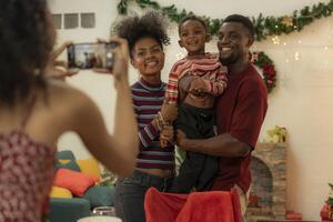 A joyful family gathers around the dinner table celebrating Christmas. The father, dressed in a Santa hat, gives a gift to the child, while everyone smiles with warmth and festive decorations. photo