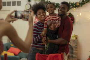 A joyful family gathers around the dinner table celebrating Christmas. The father, dressed in a Santa hat, gives a gift to the child, while everyone smiles with warmth and festive decorations. photo
