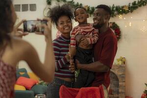 A joyful family gathers around the dinner table celebrating Christmas. The father, dressed in a Santa hat, gives a gift to the child, while everyone smiles with warmth and festive decorations. photo