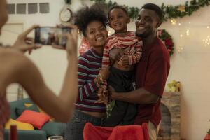 A joyful family gathers around the dinner table celebrating Christmas. The father, dressed in a Santa hat, gives a gift to the child, while everyone smiles with warmth and festive decorations. photo