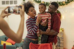 A joyful family gathers around the dinner table celebrating Christmas. The father, dressed in a Santa hat, gives a gift to the child, while everyone smiles with warmth and festive decorations. photo