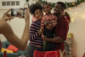 A joyful family gathers around the dinner table celebrating Christmas. The father, dressed in a Santa hat, gives a gift to the child, while everyone smiles with warmth and festive decorations. photo