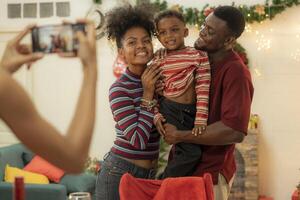 A joyful family gathers around the dinner table celebrating Christmas. The father, dressed in a Santa hat, gives a gift to the child, while everyone smiles with warmth and festive decorations. photo