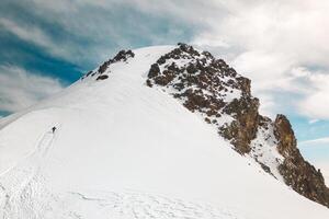 Aerial view group of climbers two above clouds climb reaching famous Mount kazbek peak in Georgia. Mount Kazbek or Mount Kazbegi is dormant stratovolcano - major mountains of the Caucasus.Summit push photo