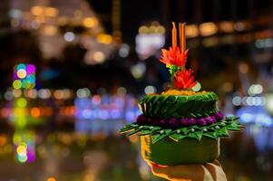 Hand holding krathong for Thailand Loy Krathong festival with colorful bokeh lights background. photo