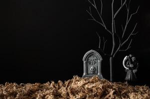 Halloween background with tombstone that have black tree and blurred ghost with dried grass on black background. Minimal concept. photo