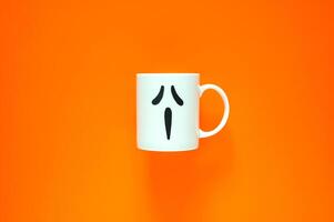 Halloween background with a coffee cup with eye and mouth stickers puts on orange background. Minimal concept. photo