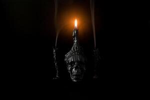 Halloween background with skull that have light candle on it with another candles that have smoke on black background. Minimal concept. photo