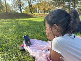 Asian little girl on the grass using phone in outdoor making call photo
