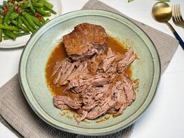 Pulled beef. Juicy and tender beef stewed with herbs and spices in a plate on the table. Slow cooked beef. photo