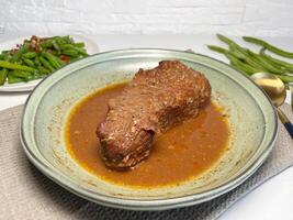 Beef stewed with herbs and spices in a plate on the table with stir fry green beans. Slow cooked beef. photo