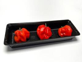 Habanero red hot chili peppers in a black plastic box on a white background, isolated on white background photo