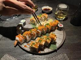 A plate of various types of sushi, including salmon, tuna, and some vegetarian options, served with soy sauce on wooden table photo